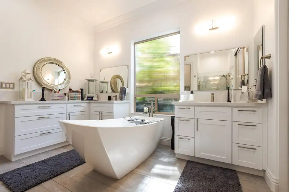 Bathroom remodeling Sacramento project by Thrive Home Construction: primary bath with a sculpted freestanding tub between two white shaker vanities with quartz tops