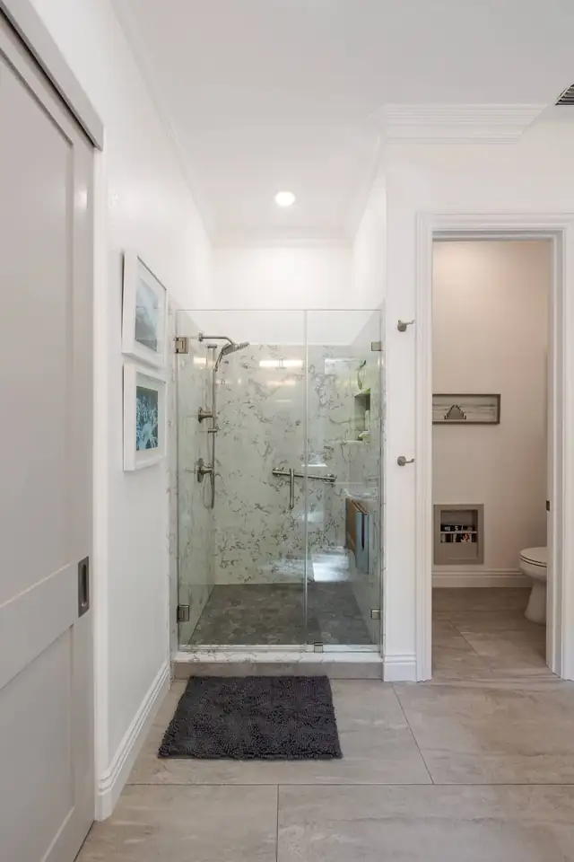 Walk-in shower with frameless glass door, white marble-look walls and a dark pebble shower floor