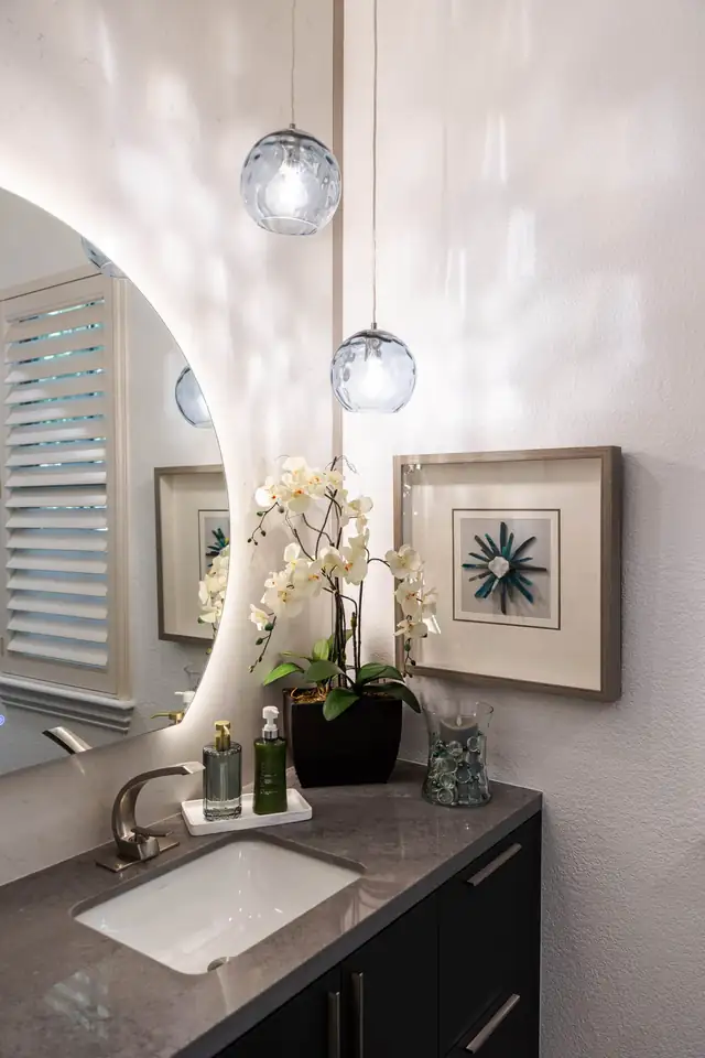 Bathroom vanity with gray quartz top, undermount sink, round backlit mirror and blue glass pendant lights