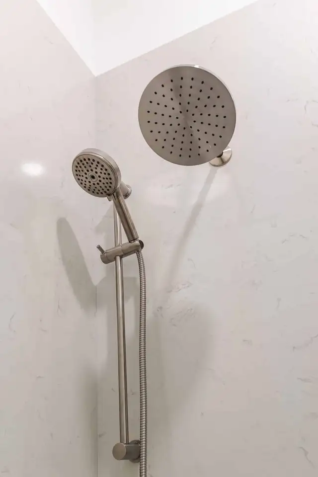 Brushed nickel rain showerhead and handheld shower on a slide bar against white marble-look walls