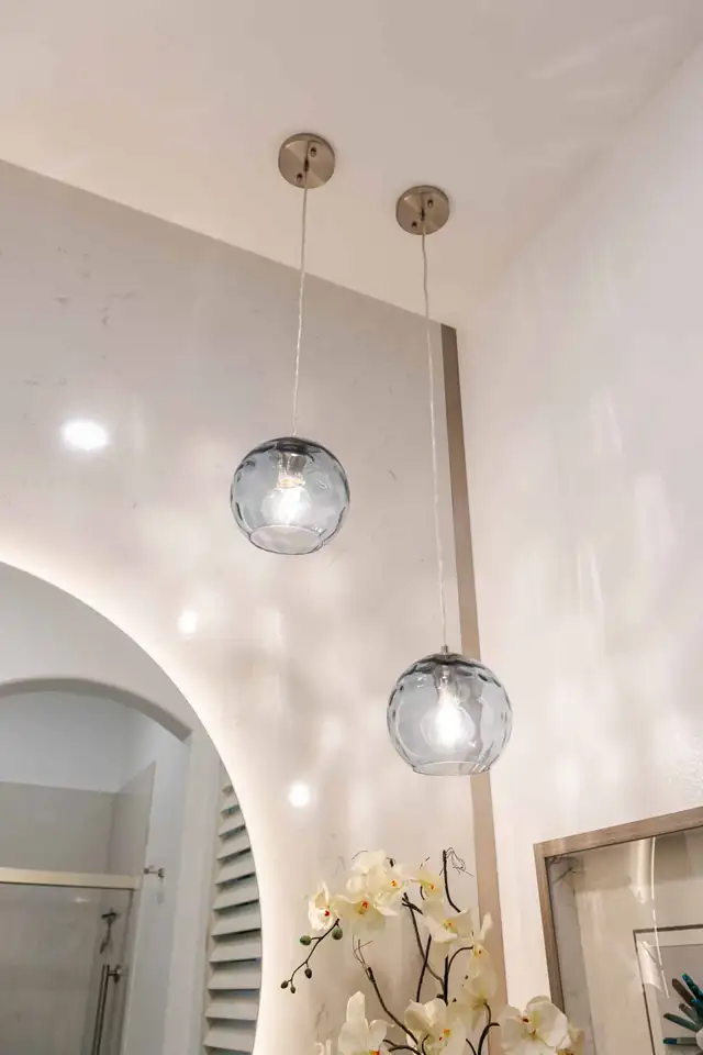Arched backlit mirror framed by two hand-blown glass pendants in a remodeled bathroom