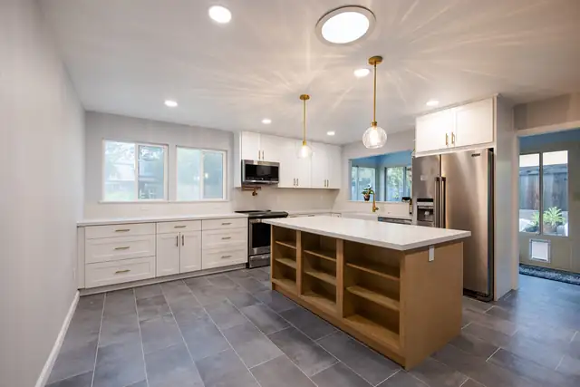 Remodeled kitchen with white shaker cabinets, wood island with open shelving, quartz counters and gray tile floor