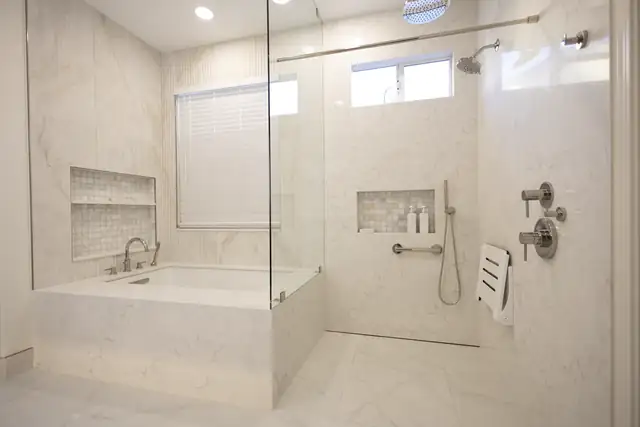 Bathroom by Thrive Home Construction with a white soaking tub and a walk-in glass shower in matching marble-look tile, wall niches and a fold-down shower seat