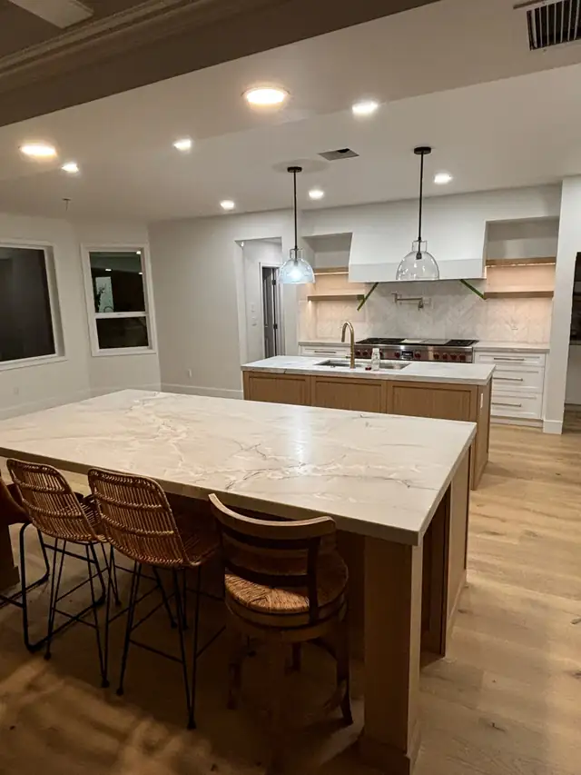 Kitchen remodel with large veined quartz island, woven counter stools, wood island base and light oak floors