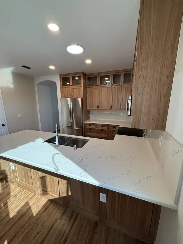 Kitchen with quartz peninsula and undermount sink, natural wood cabinets and stainless refrigerator